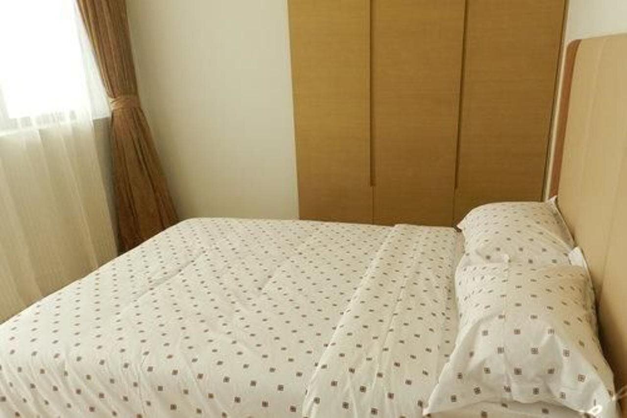 Una habitación de hotel con una cama, cabecera de madera y cortinas traslúcidas.