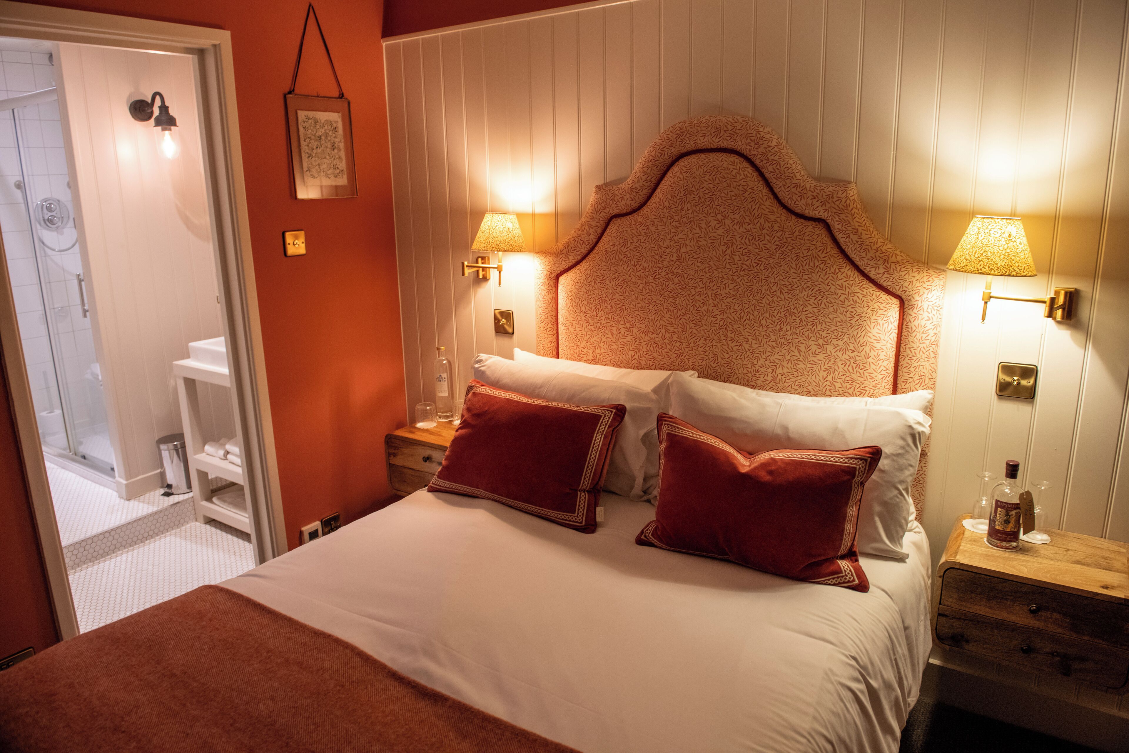 Habitació d'hotel amb un llit gran, dues làmpades de nit, una taula de nit de fusta i un bany visible a través d'una porta oberta.
