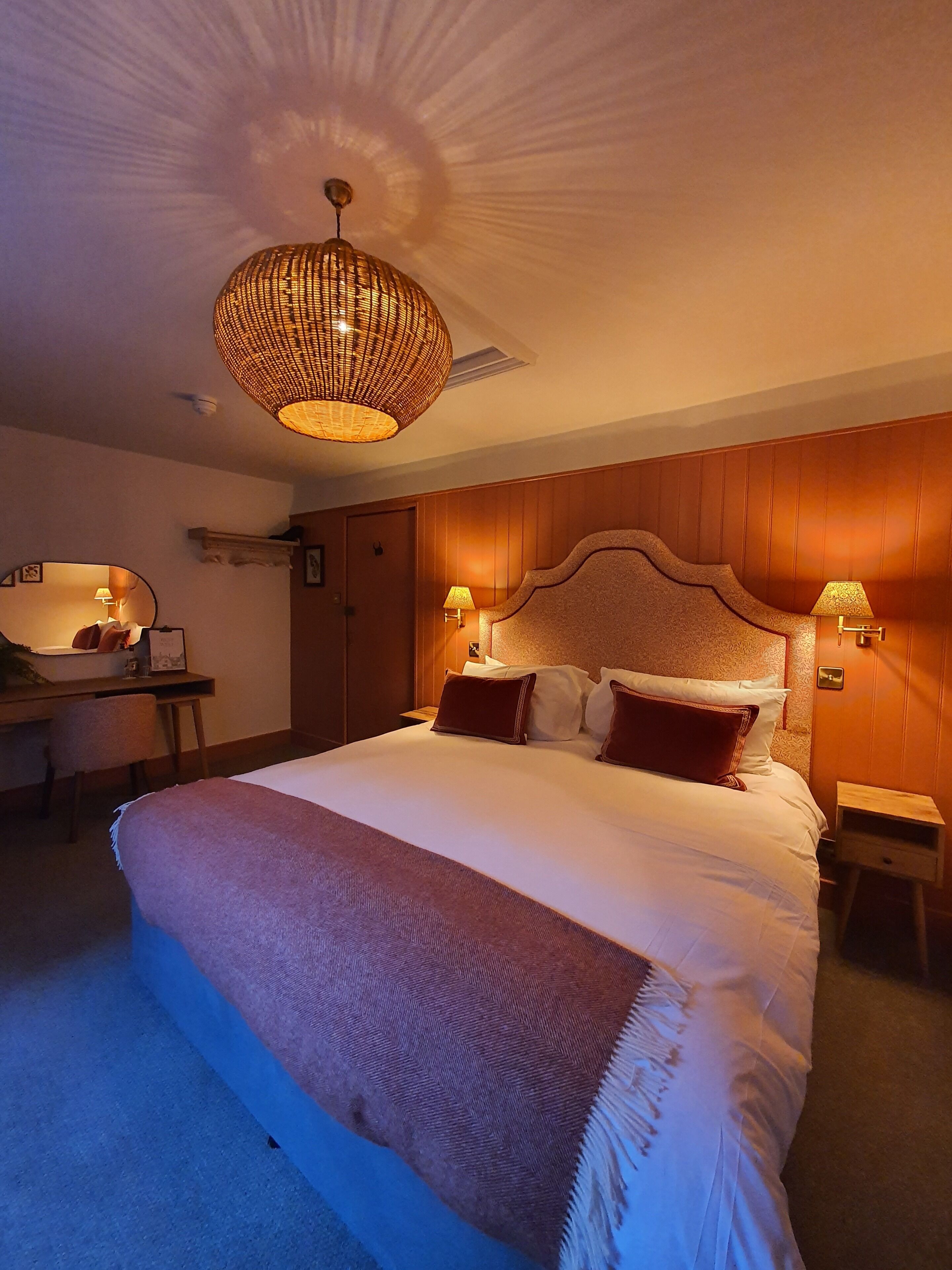 Een slaapkamer met een groot bed, een bureau, een stoel, een spiegel en een hanglamp.