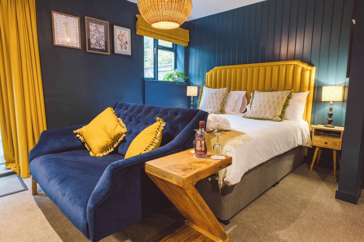 A room with a bed, a sofa, a wooden nightstand, and a window with curtains.