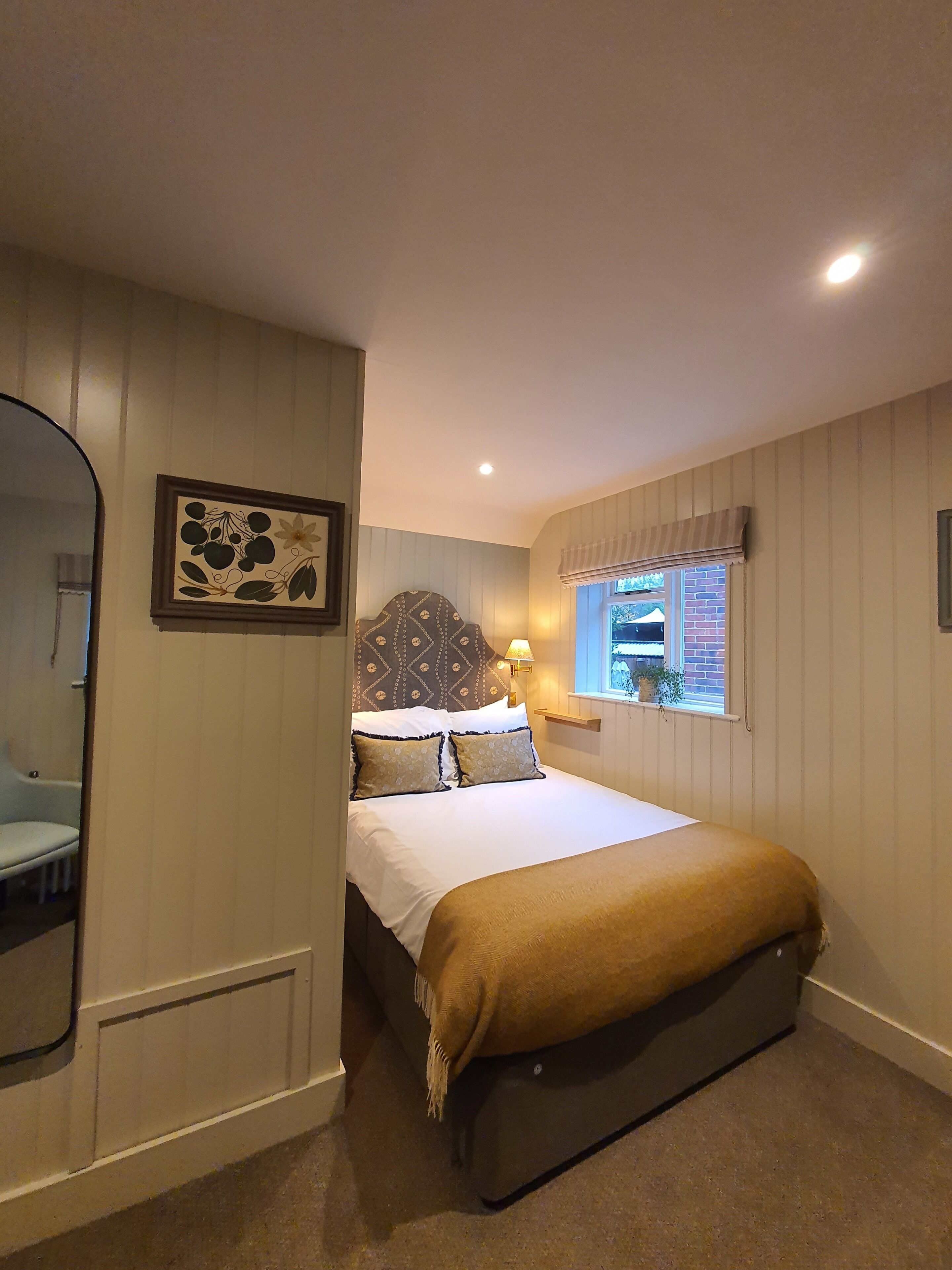 A bedroom with a bed, a bedside lamp, a window with a view, and a mirror.