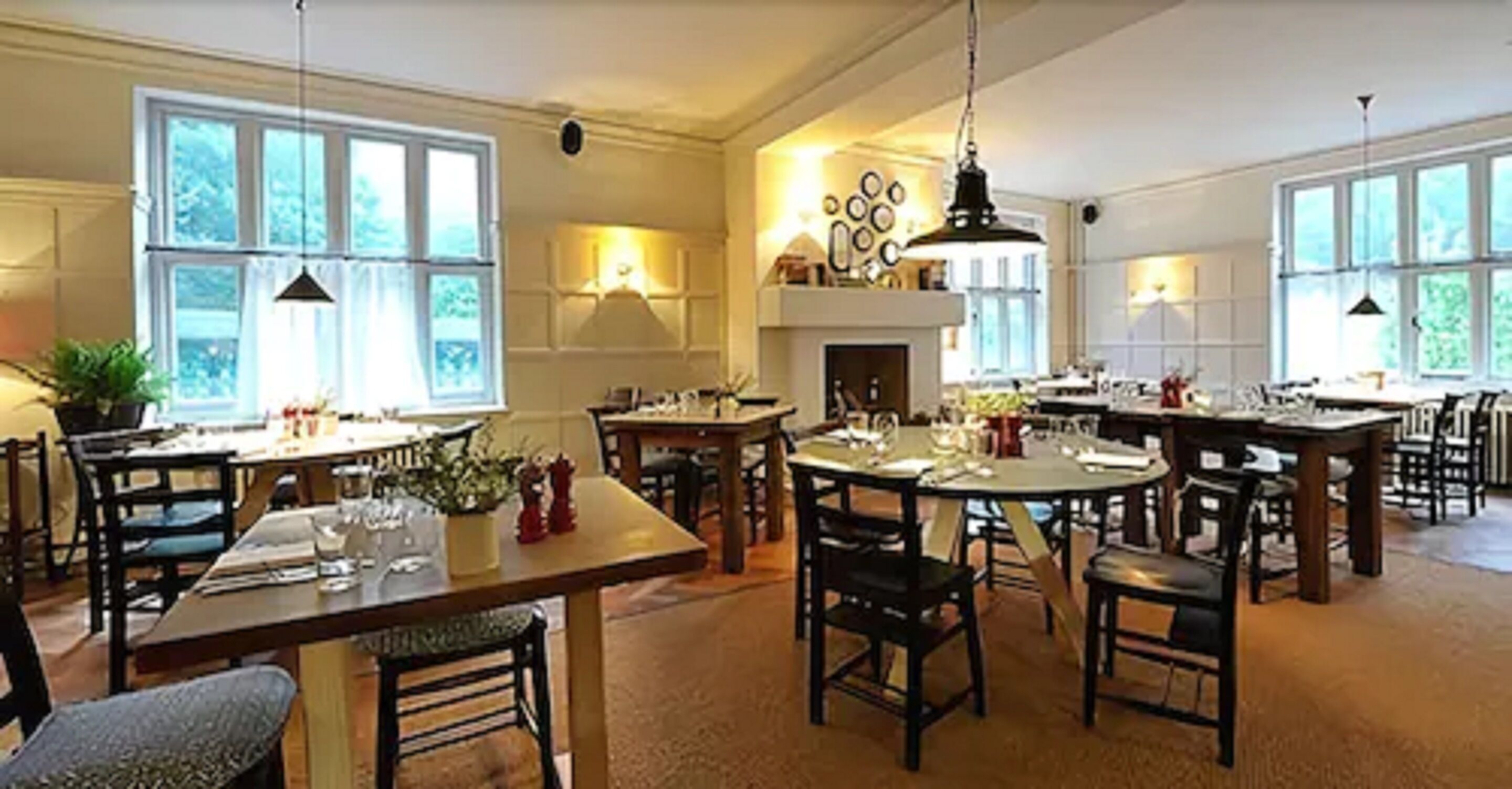 A spacious dining area with multiple tables and chairs, large windows, and a fireplace.