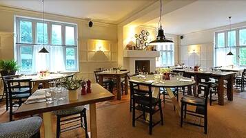A spacious dining area with multiple tables and chairs, large windows, and a fireplace.