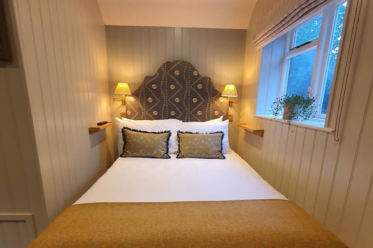 A bedroom with a bed, headboard, bedside lamps, window, and curtains.
