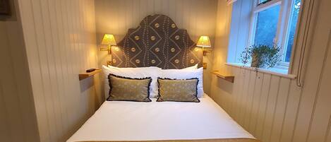 A bedroom with a bed, headboard, bedside lamps, window, and curtains.