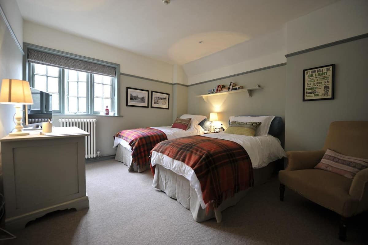 A bedroom with two beds, a chair, a radiator, and a window.