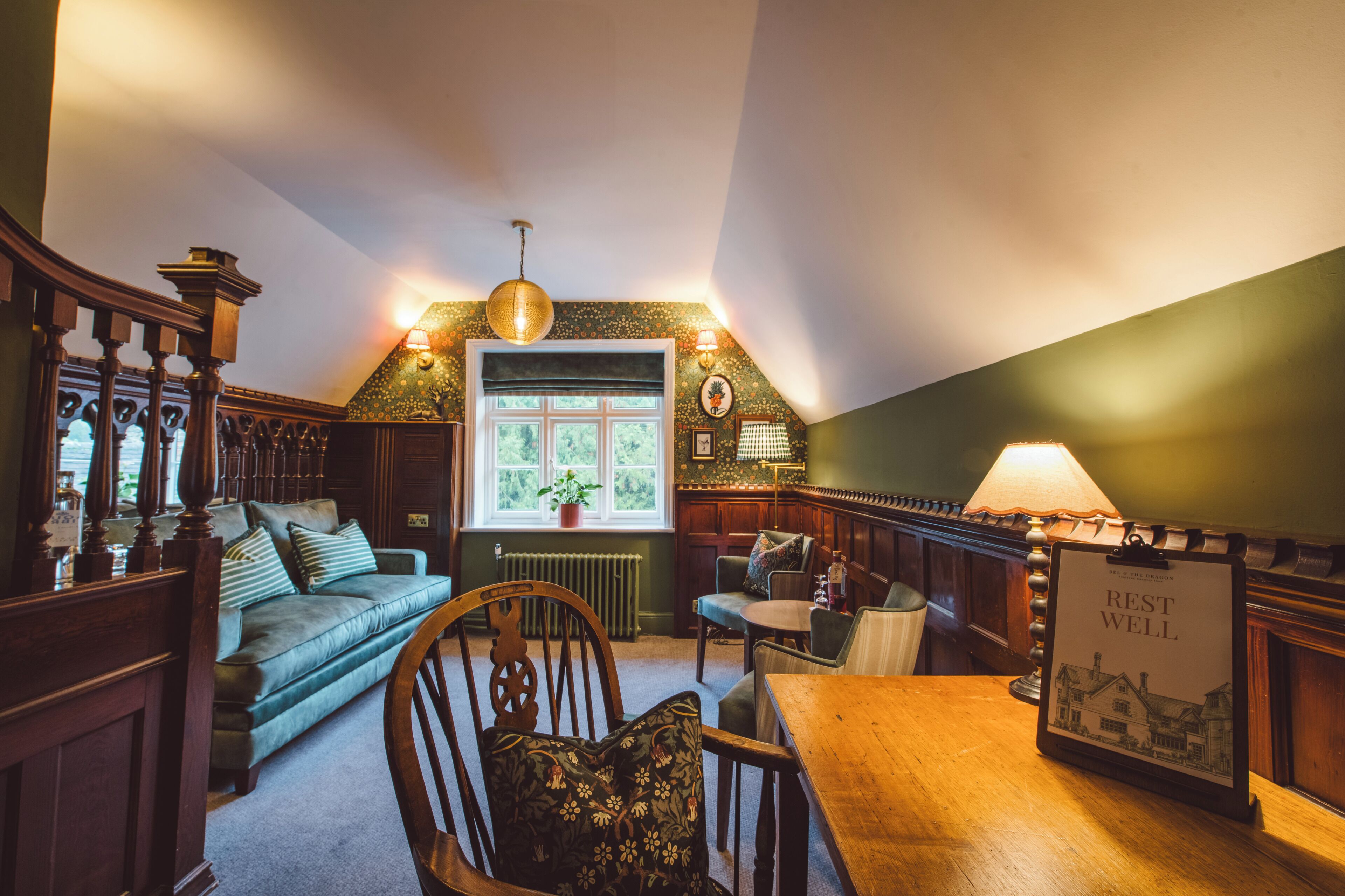 A cozy room with a wooden table, a green sofa, a wooden chair, and a lamp.