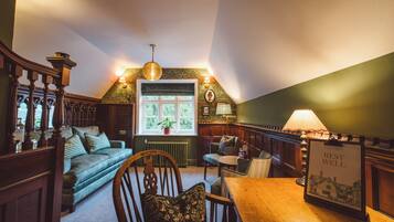 A cozy room with a wooden table, a green sofa, a wooden chair, and a lamp.