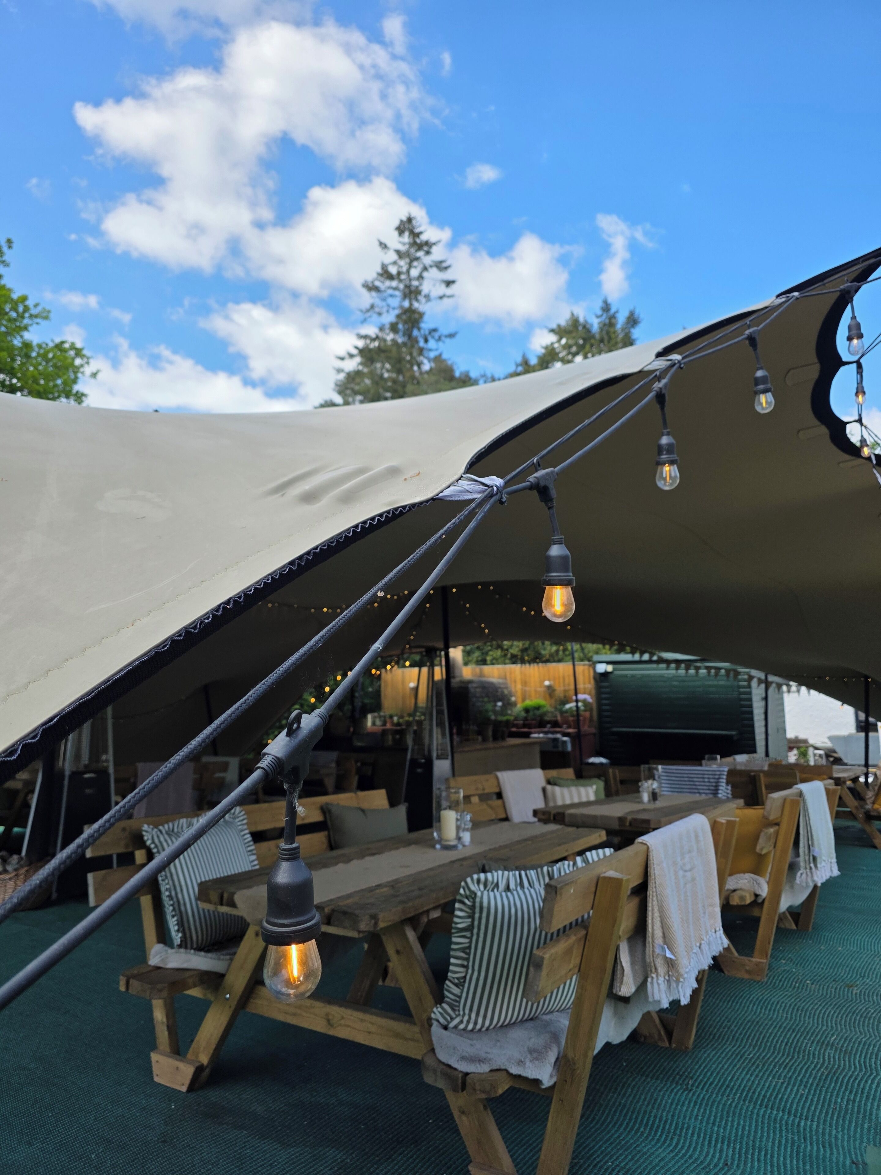 A tent with a table and chairs, string lights, and a view of the outdoors.