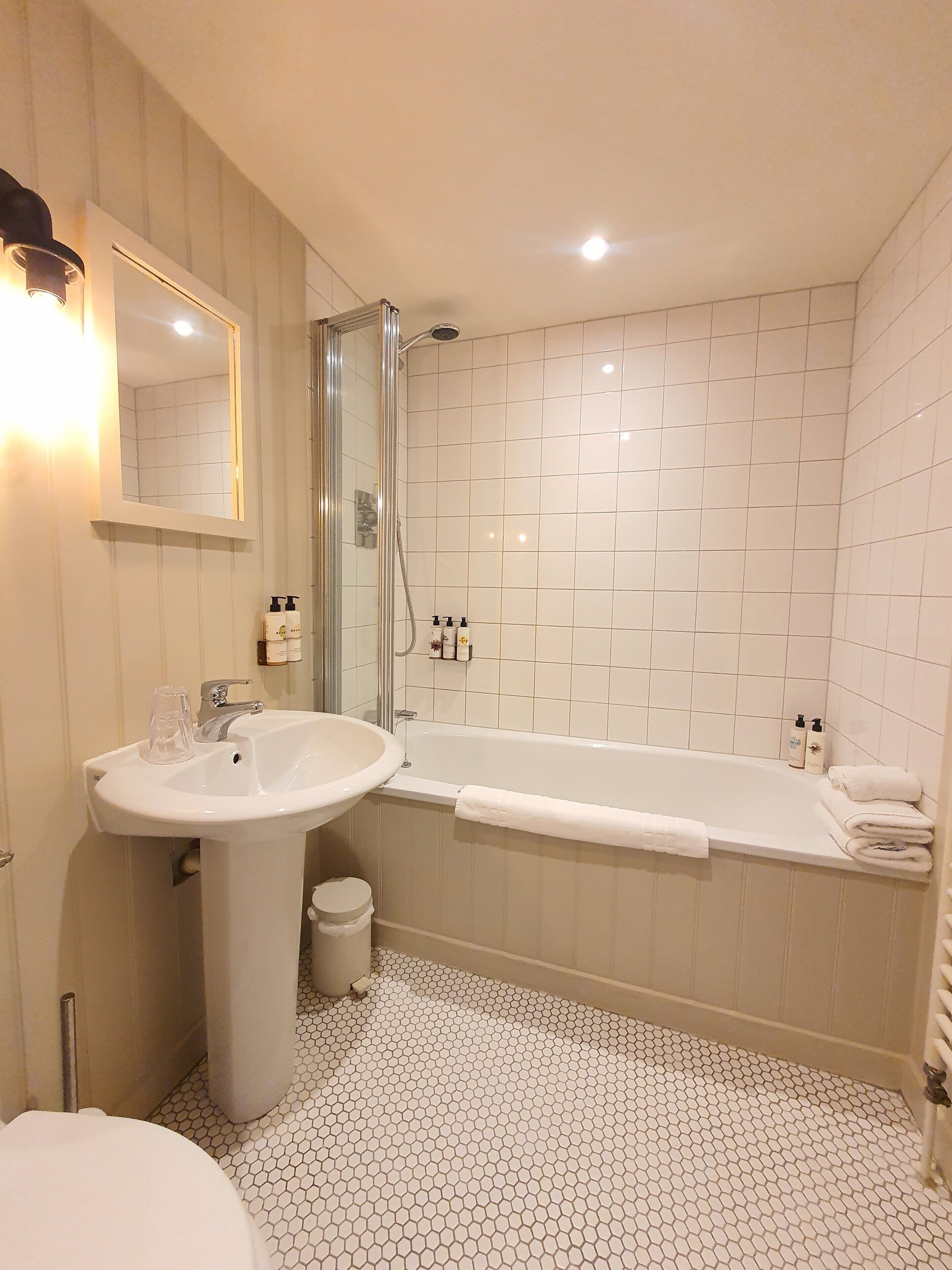 Une salle de bain avec un lavabo, un miroir, une douche et un sol carrelé.