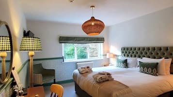 A hotel room with a large bed, a bedside table with a mirror, a chair, and a window with a view of greenery.