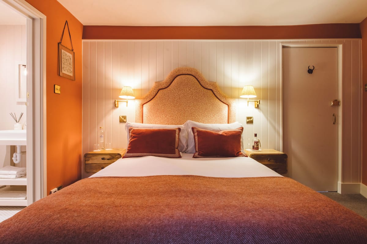 A hotel room with a large bed, two bedside tables with lamps, a wooden headboard, and a door with a handle.
