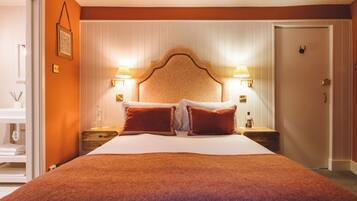 Habitación de hotel con una cama grande, dos mesitas de noche con lámparas, un cabecero de madera y una puerta con manija.