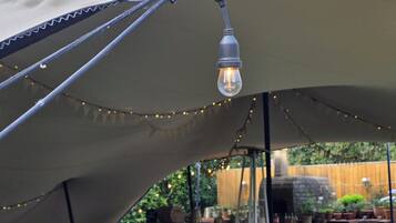 An outdoor dining area with wooden tables and benches, string lights, and a canopy overhead.