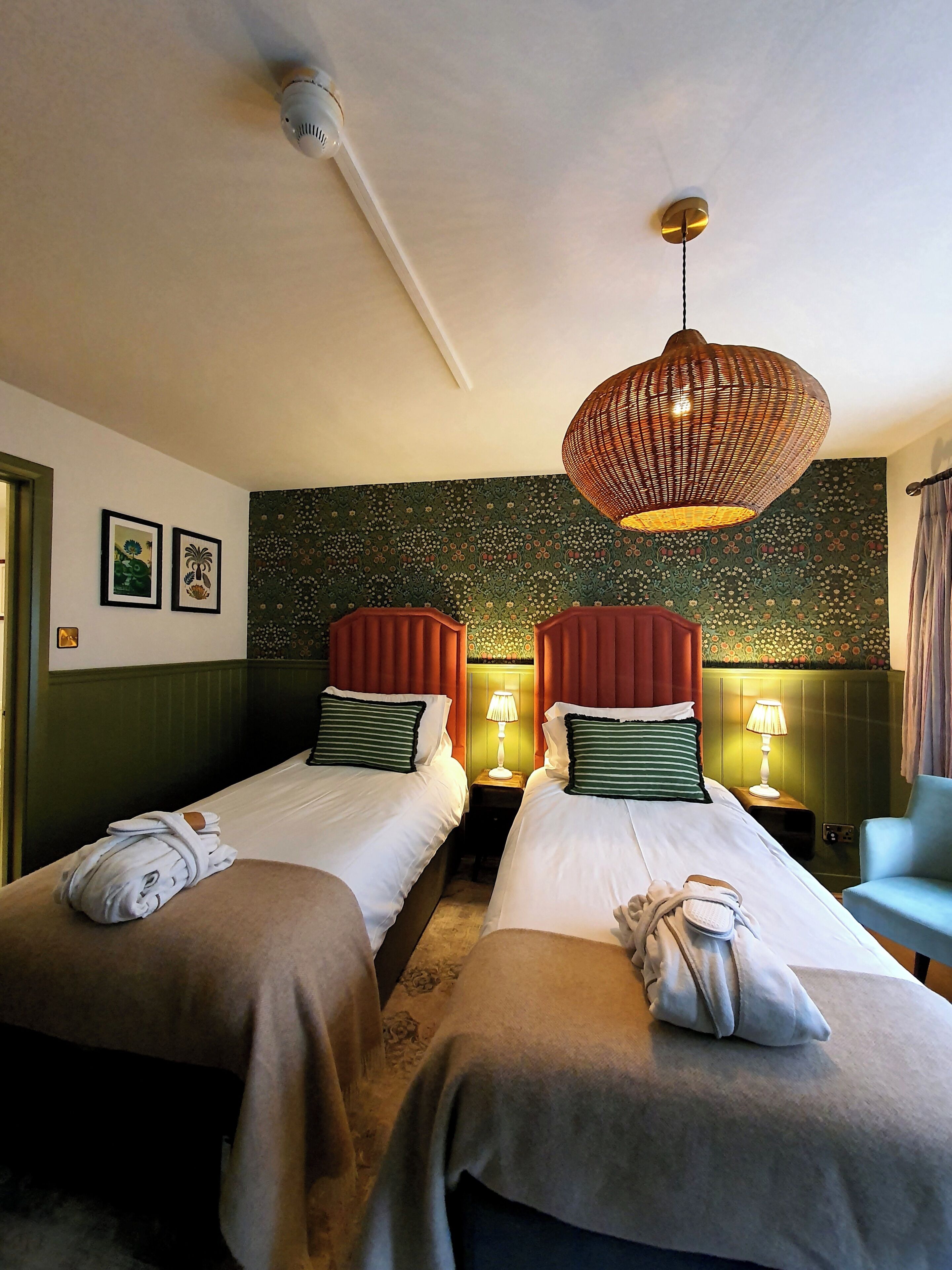 Een hotelkamer met twee bedden, een hanglamp en een bloemenpatroon op de muur.