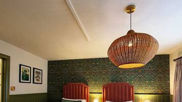Een hotelkamer met twee bedden, een hanglamp en een bloemenpatroon op de muur.