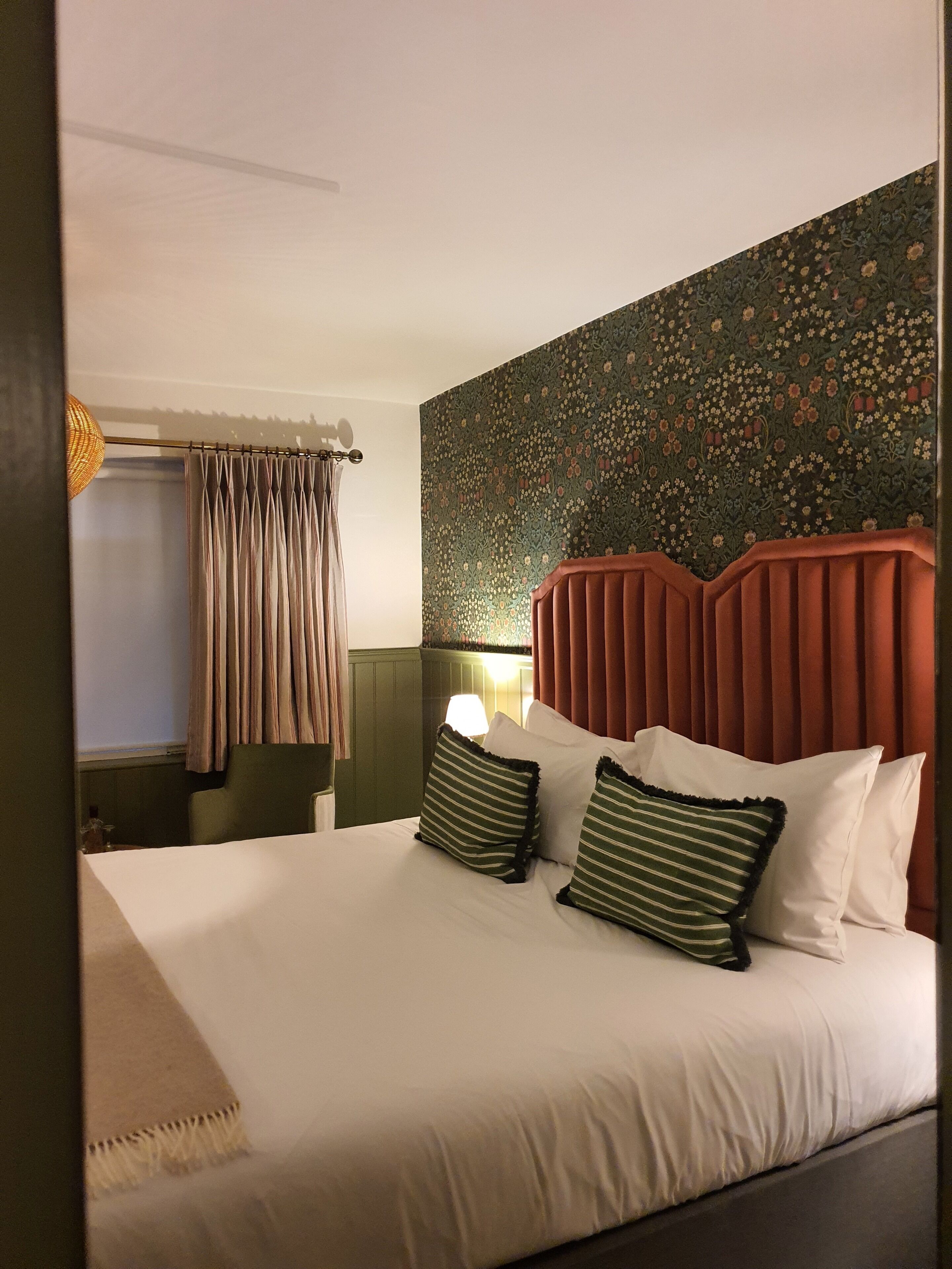 Een hotelkamer met een bed, gordijnen, een hoofdeinde en een wand met bloemenpatroon.