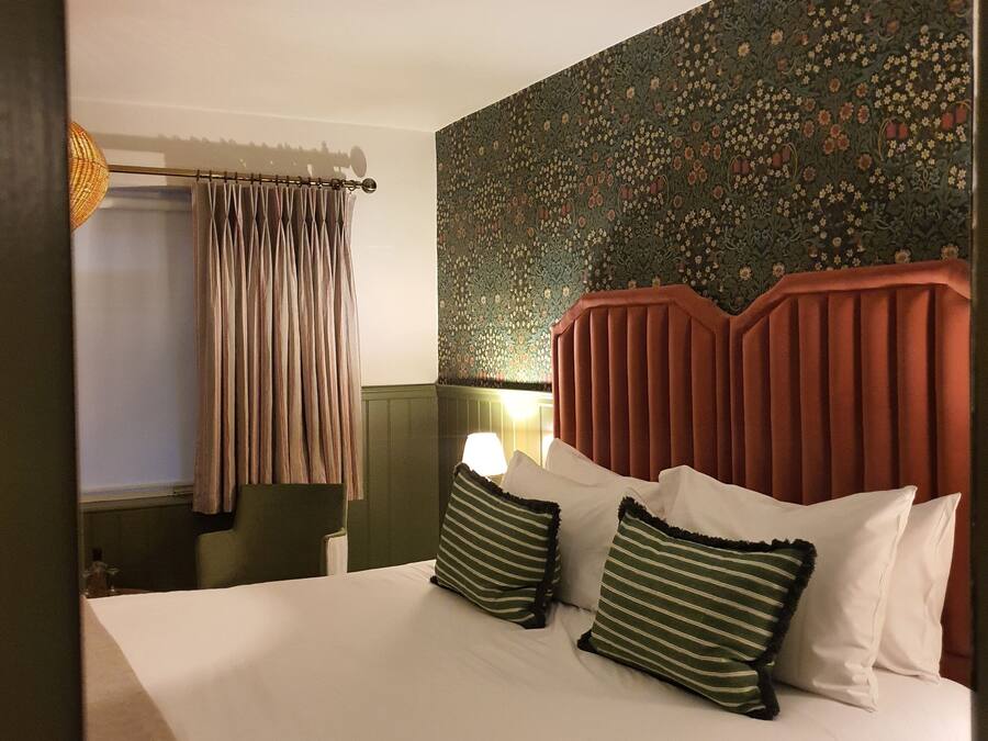 Een hotelkamer met een bed, gordijnen, een hoofdeinde en een wand met bloemenpatroon.