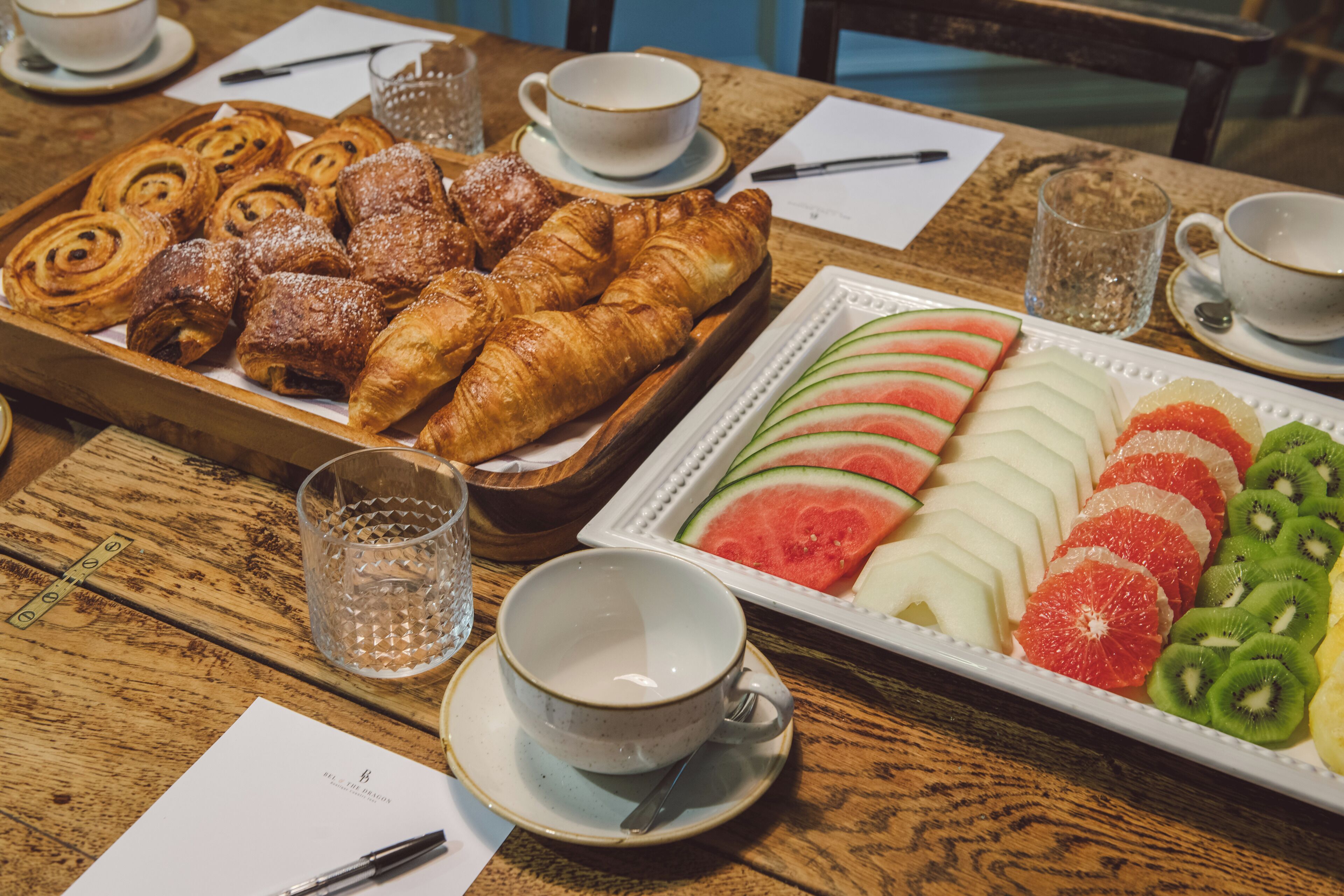 Un bufé de desayuno con pasteles, frutas y bebidas sobre una mesa de madera.