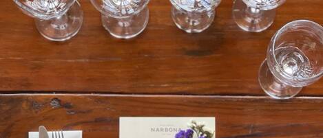 Una mesa de madera con seis vasos vacíos, una servilleta doblada con un tenedor y un menú decorado con una flor.