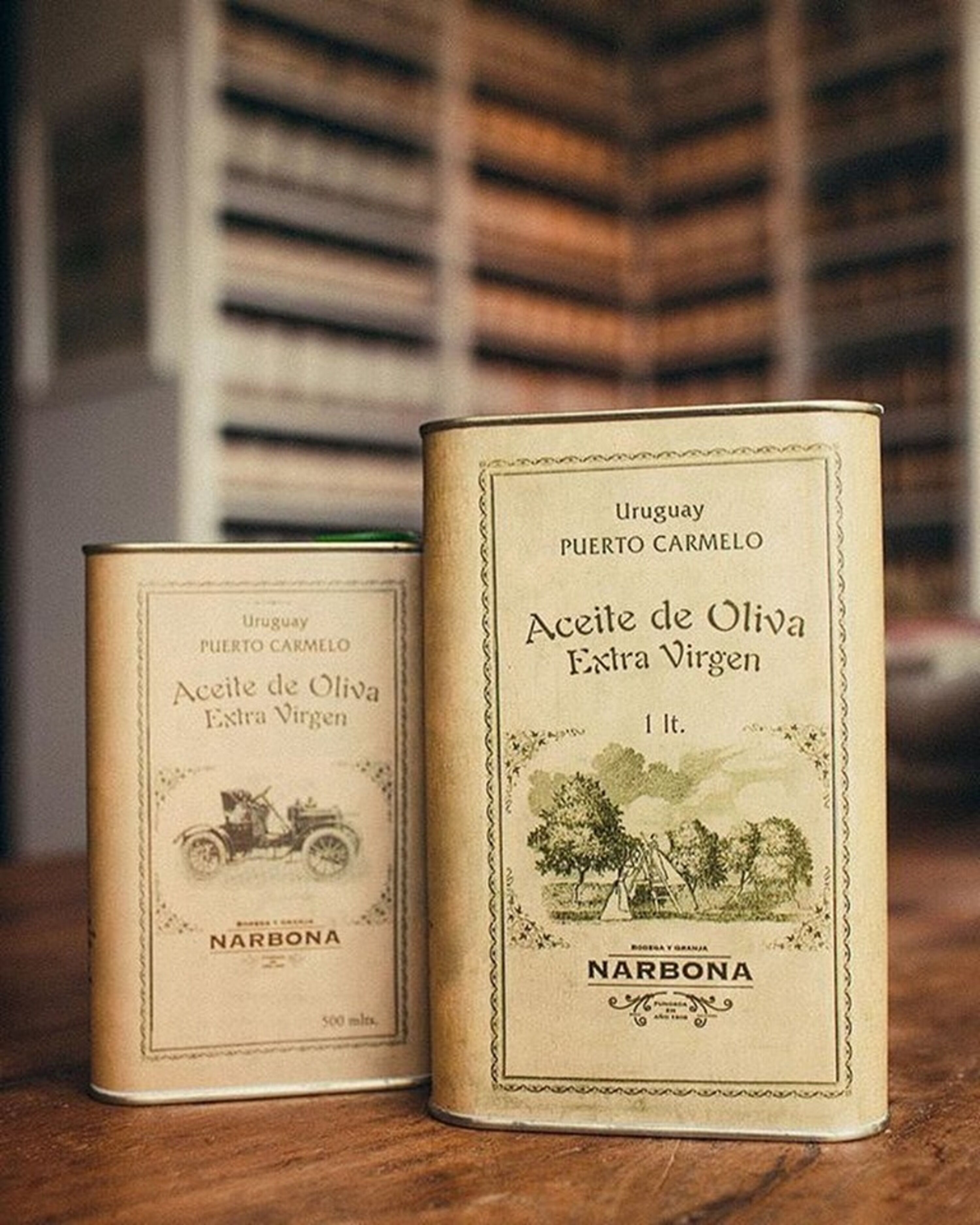 Two vintage-style tin containers labeled 'Uruguay PUERTO CARMELO' and 'Aceite de Oliva Extra Virgin' with a rustic design and a small illustration of a landscape.