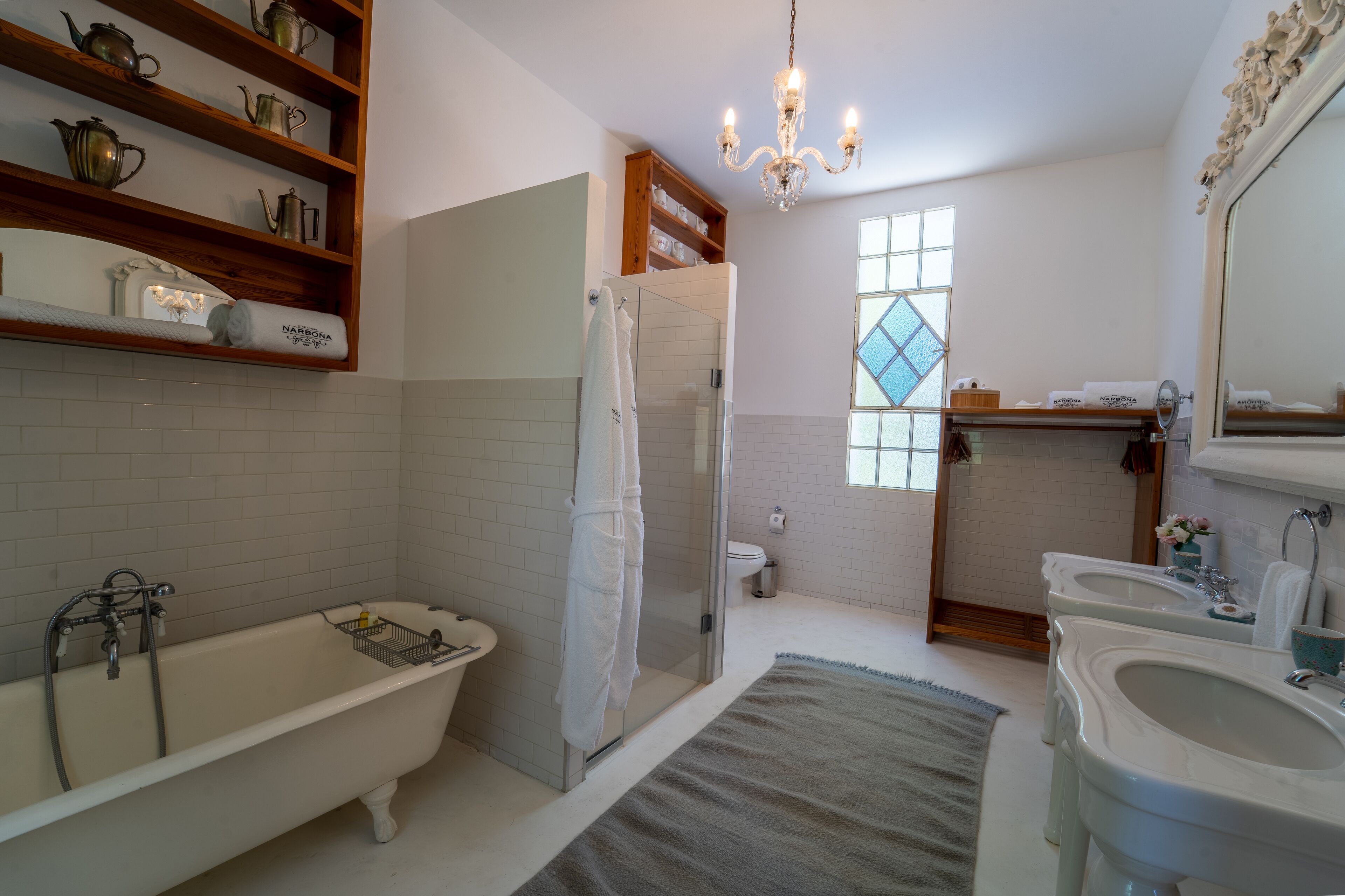 A bathroom with a freestanding bathtub, a glass-enclosed shower, a vanity with two sinks, and a chandelier.