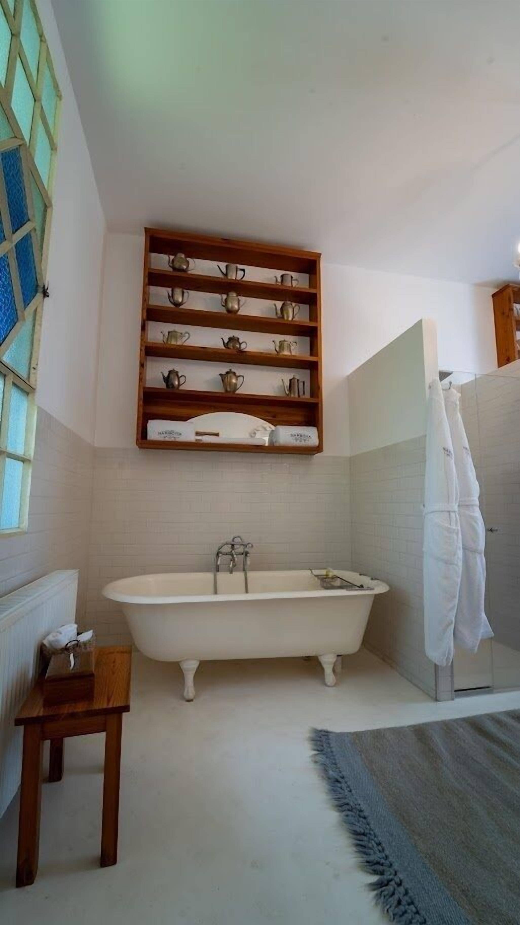 A bathroom with a freestanding bathtub, a wooden shelf with teapots, a small wooden table, and a shower area.