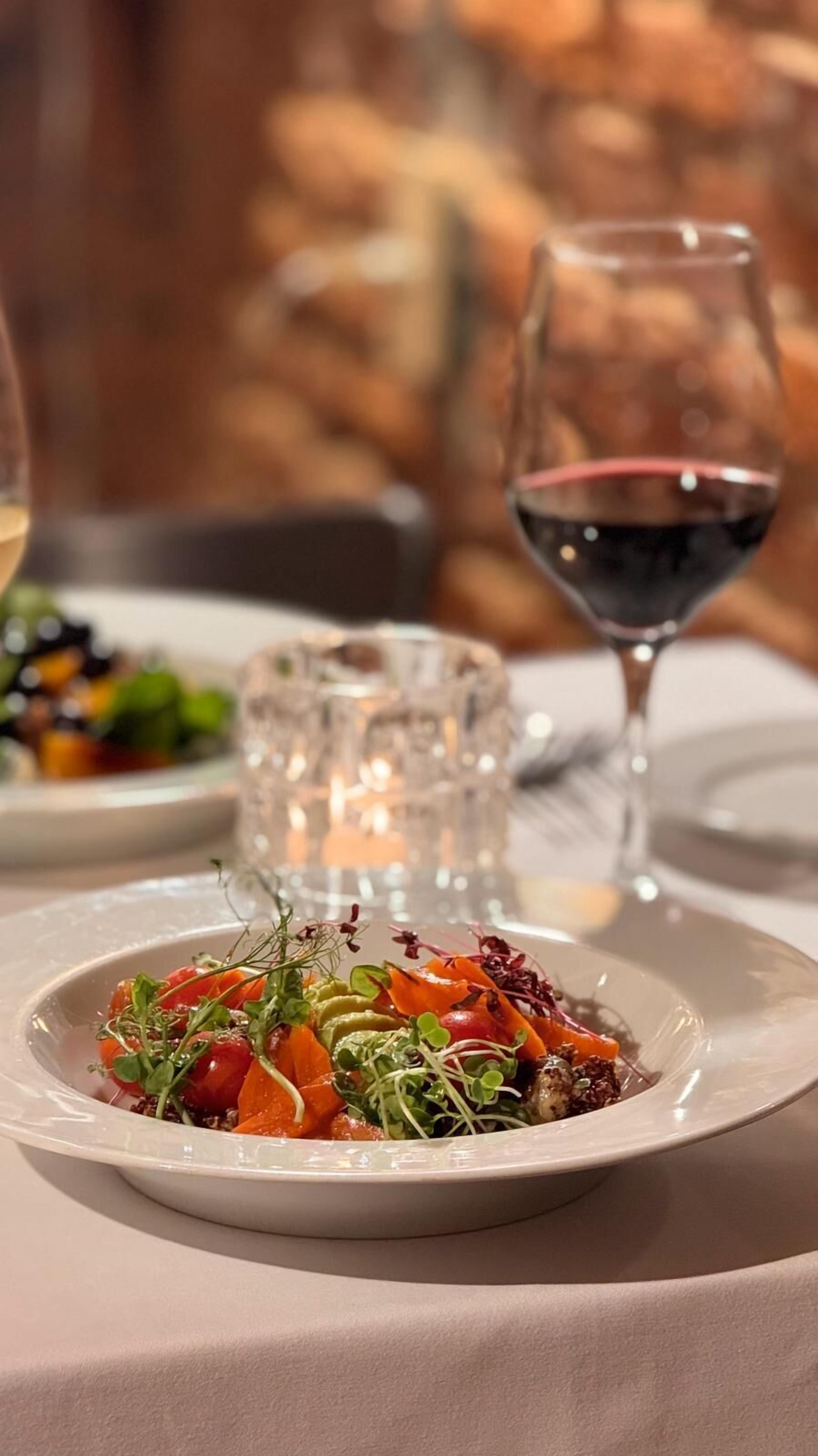 A dining table with a plate of food, a glass of red wine, and a candle.