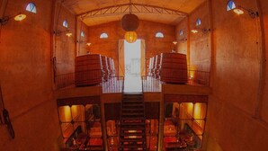 A spacious interior with a central staircase leading to a balcony, surrounded by rows of seating and wooden barrels. - Narbona Wine Lodge (Carmelo)