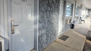 A hotel corridor with doors numbered 101 and 102, stone wall, and outdoor seating area. - Howard Johnson by Wyndham Hinton (Hinton)