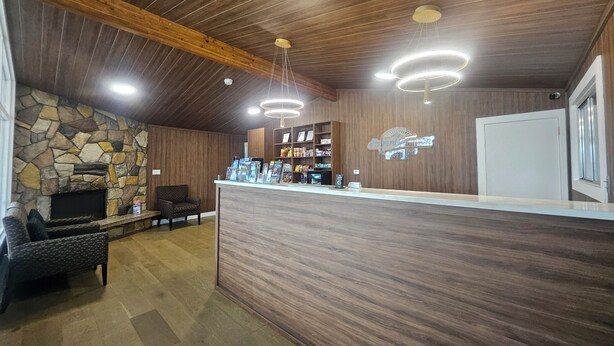 A reception area with a stone wall, wooden ceiling, and a reception desk with a sign. - Howard Johnson by Wyndham Hinton (Hinton)