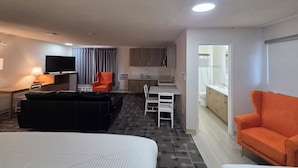 A hotel room with a bed, a sofa, a TV, a desk, a chair, and a kitchenette.