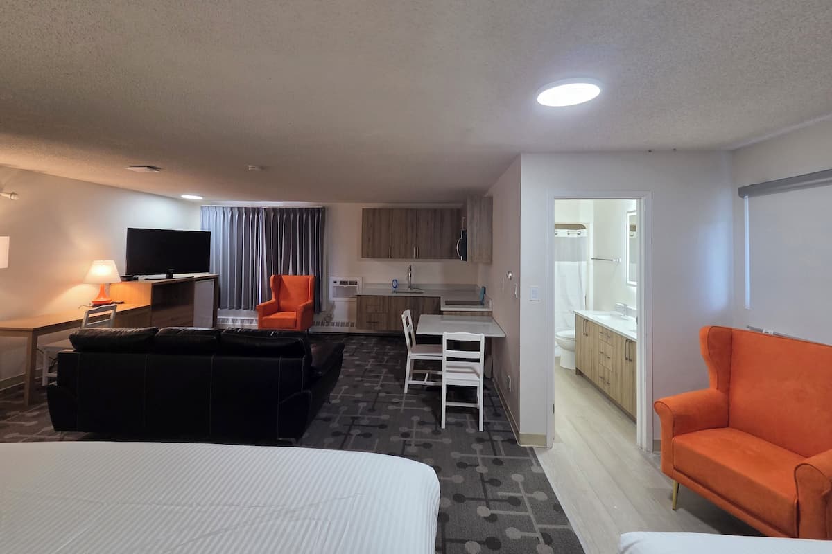 Una camera d'albergo con un letto, un divano, una televisione, una scrivania, una sedia e angolo cottura.