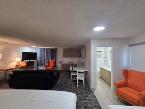 A hotel room with a bed, a sofa, a TV, a desk, a chair, and a kitchenette. - Howard Johnson by Wyndham Hinton (Hinton)