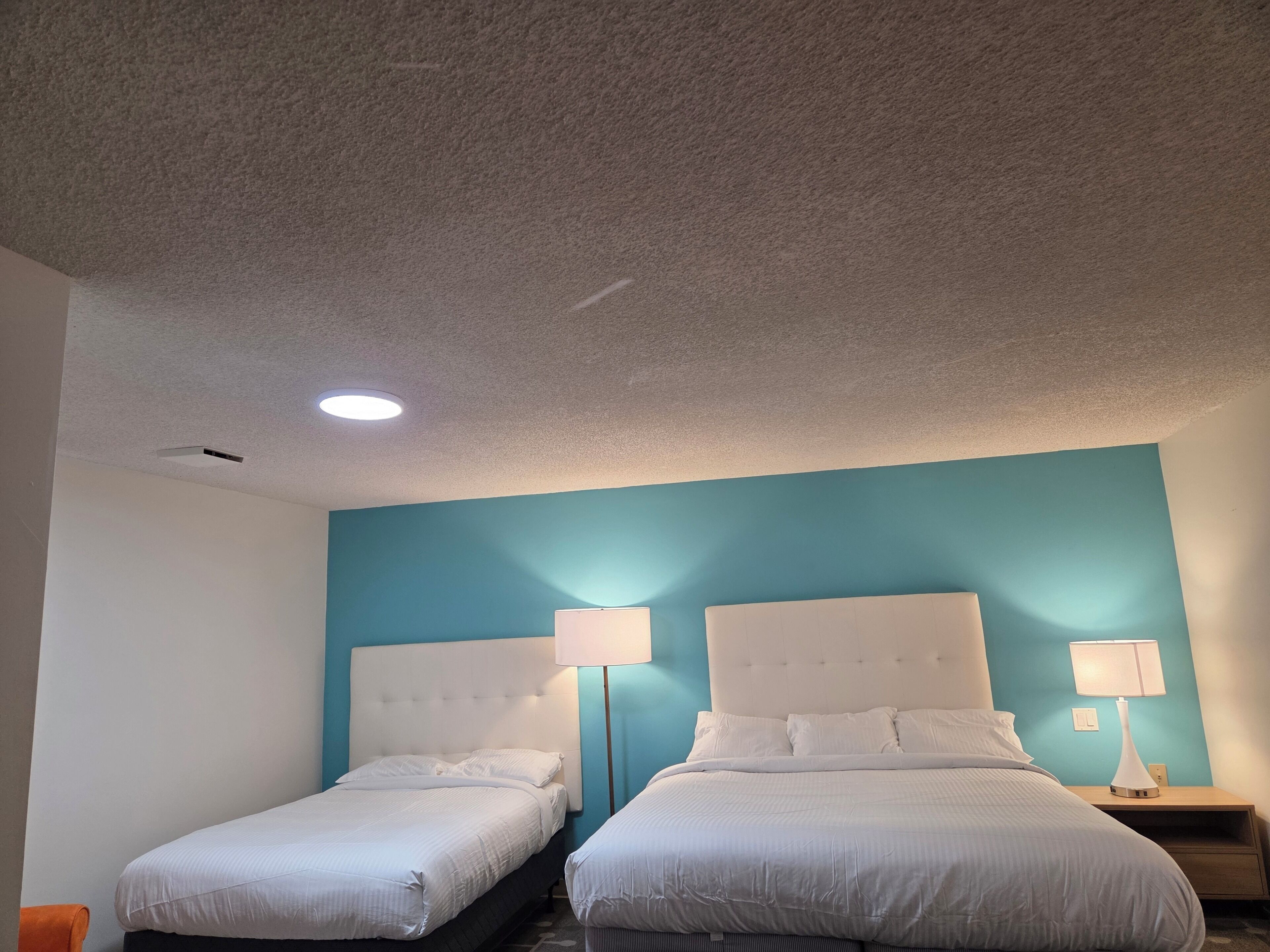 A hotel room with two beds, a ceiling light, and a wall-mounted lamp.