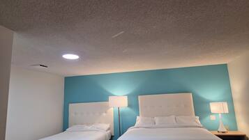A hotel room with two beds, a ceiling light, and a wall-mounted lamp.