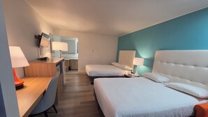 A hotel room with a desk, two beds, a chair, and a kitchenette. - Howard Johnson by Wyndham Hinton (Hinton)