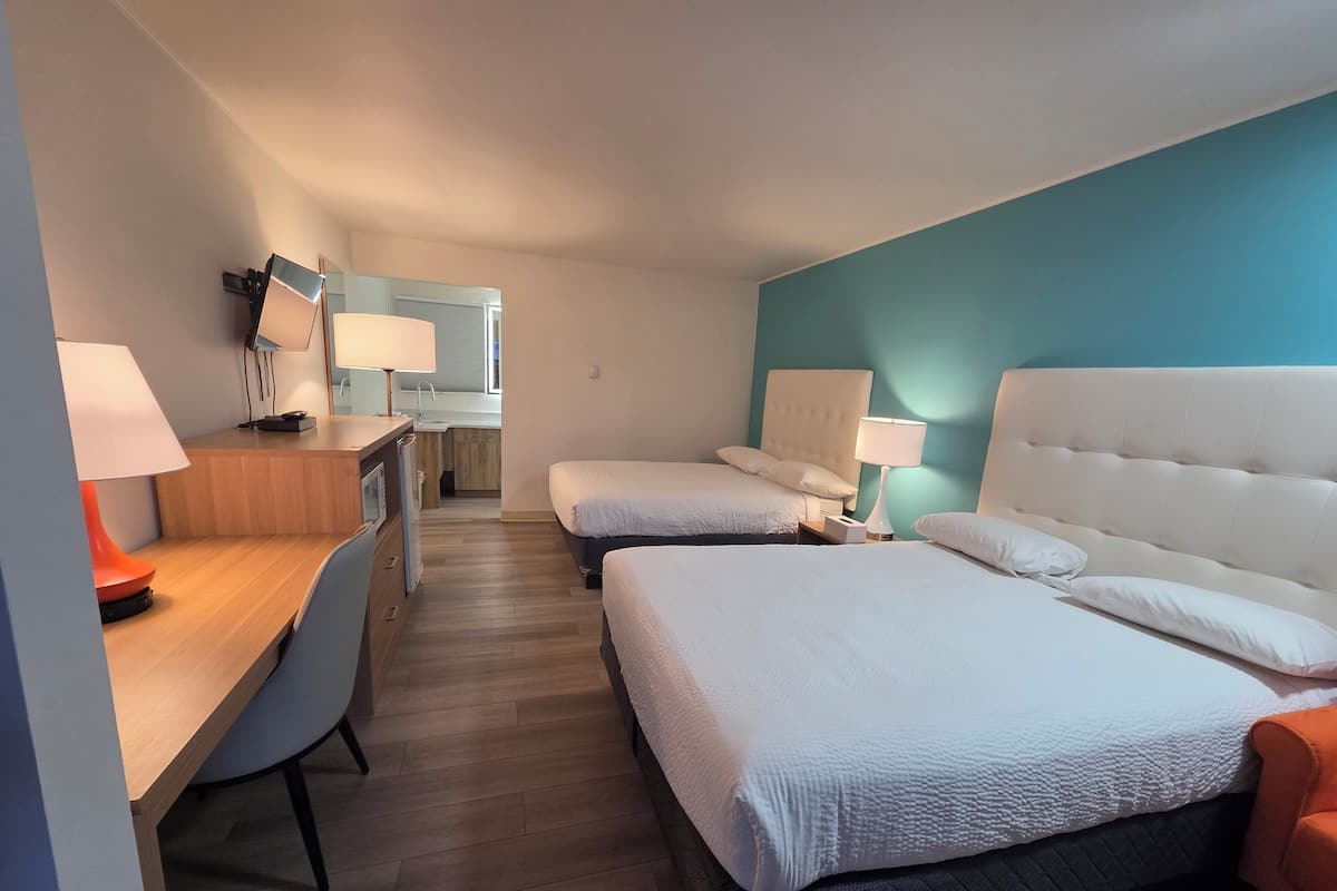 Una camera d'albergo con una scrivania, due letti, una sedia e angolo cottura.
