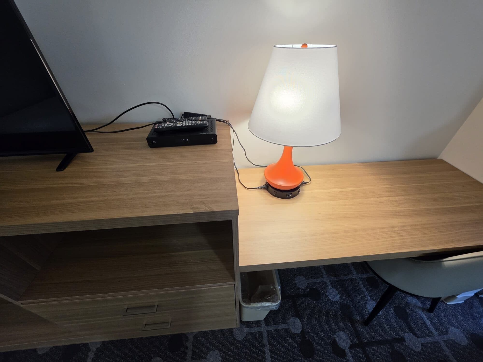 Ett skrivbord i trä med en lampa, en fjärrkontroll och en papperskorg.