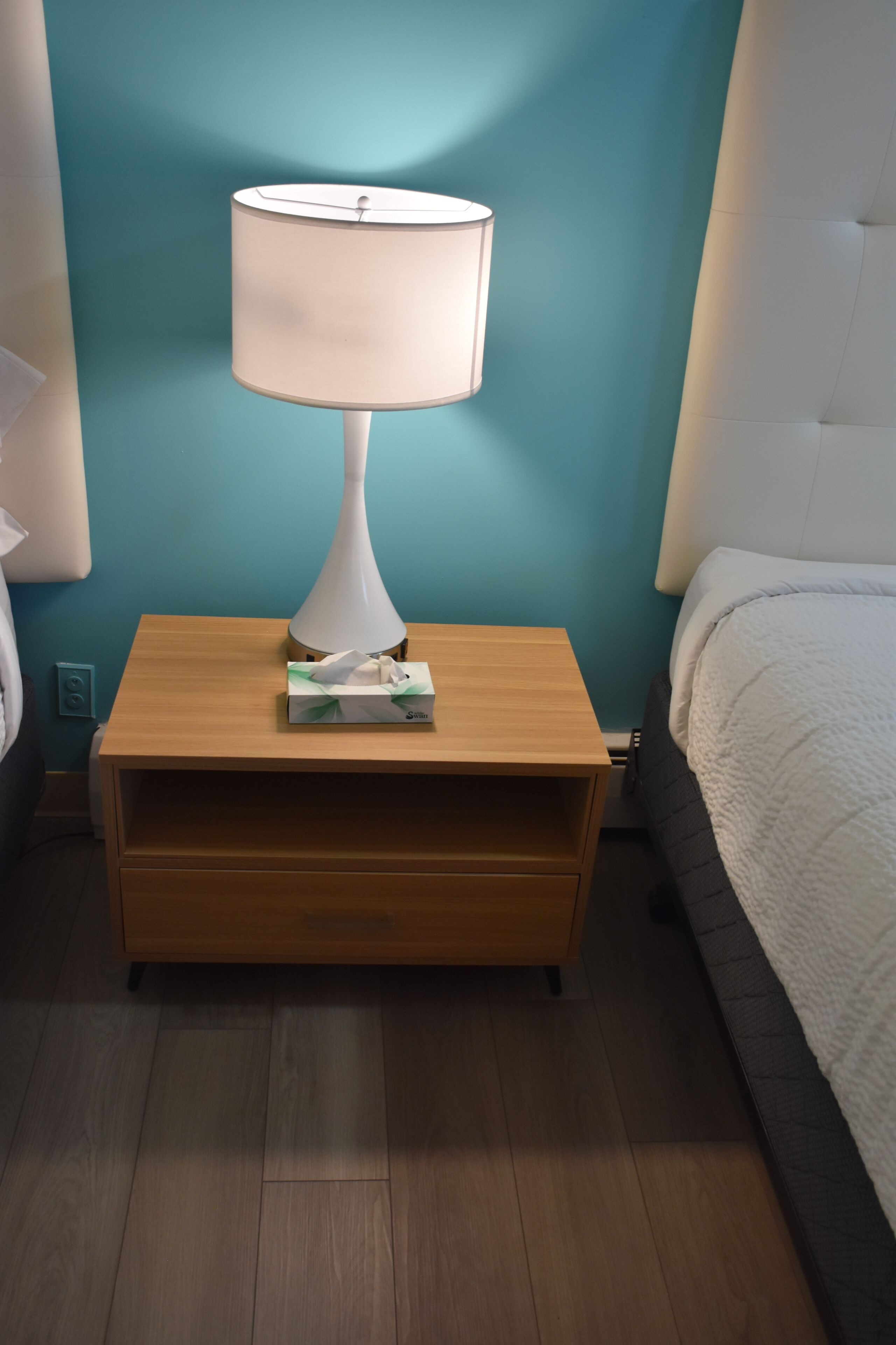 A wooden bedside table with a white lamp, a tissue box, and a drawer.