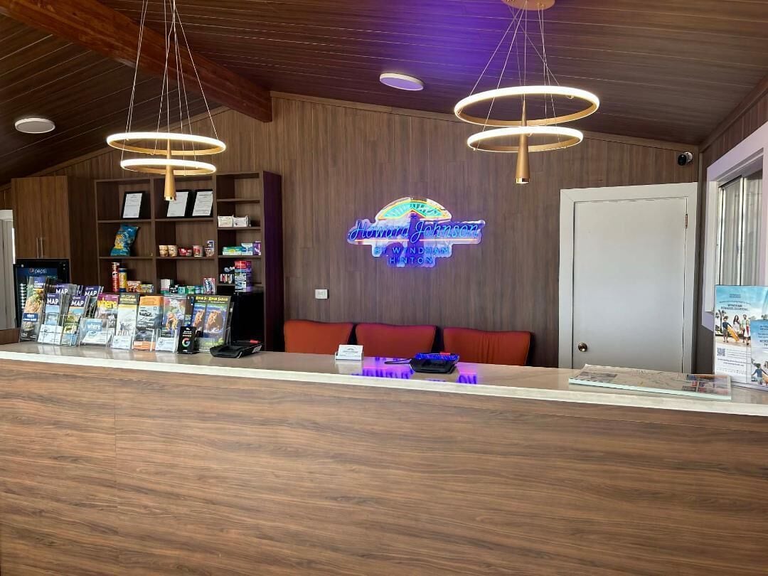 A reception desk with a wooden finish, a neon sign, and a seating area with red cushions.