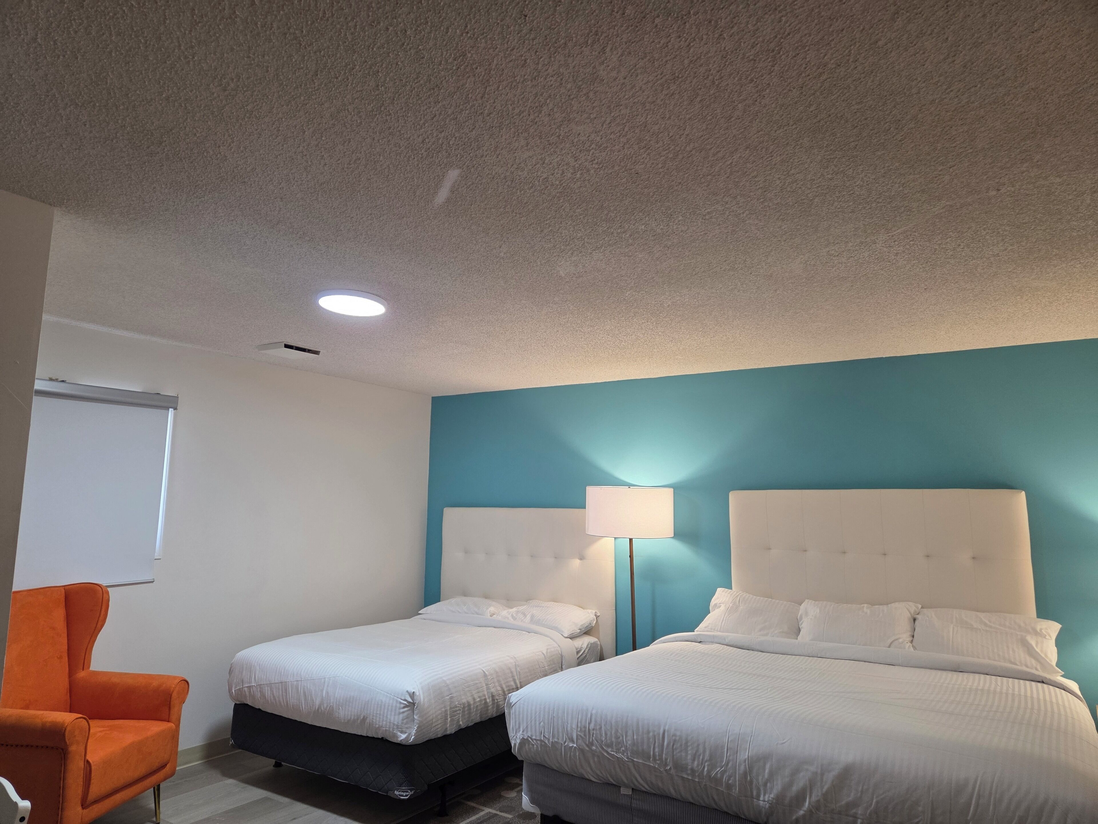 Habitación de hotel con dos camas, una silla, una lámpara y una luz en el techo.