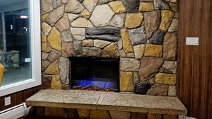 A stone fireplace with a built-in bench, a window to the left, and a stone wall. - Howard Johnson by Wyndham Hinton (Hinton)