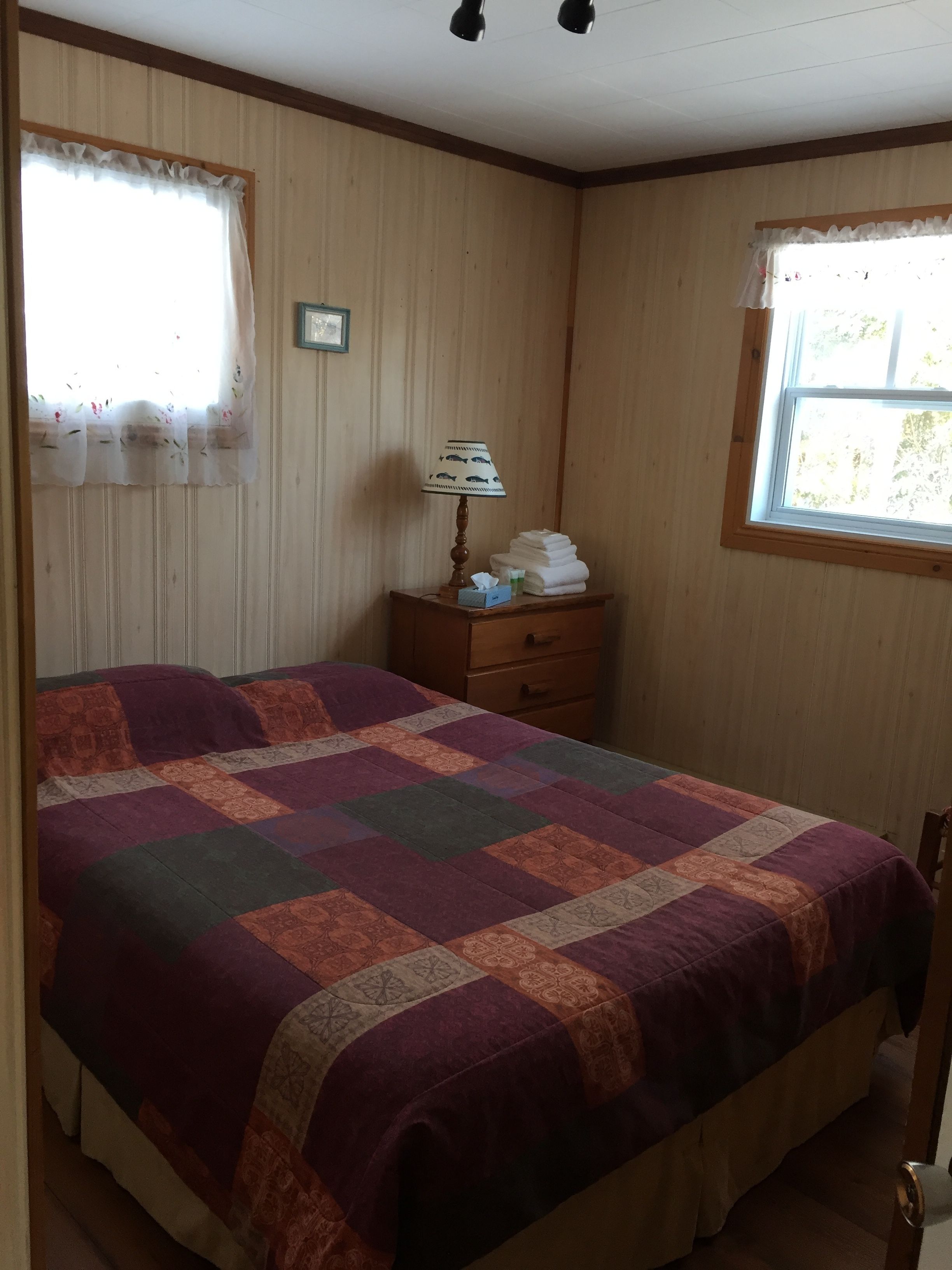 Une chambre à coucher avec un grand lit, une table de chevet avec une lampe et deux fenêtres avec des rideaux.