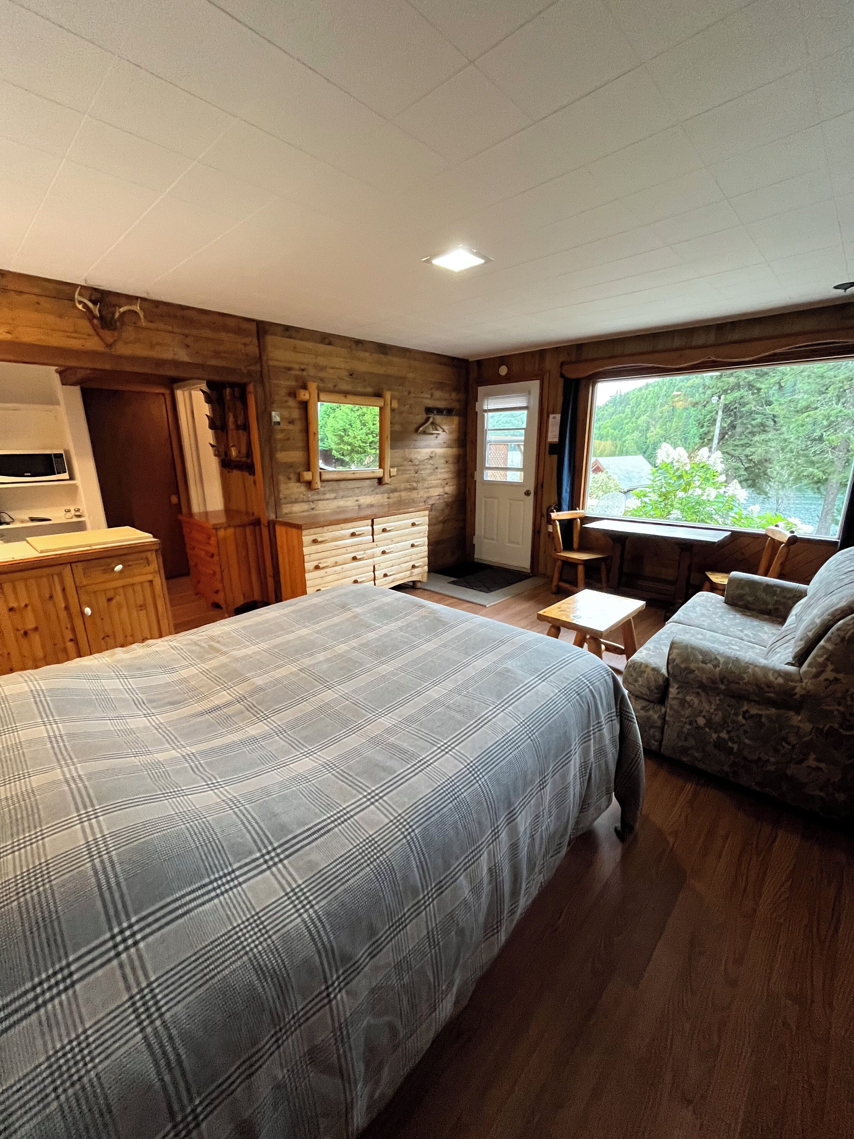 Un dormitorio con una cama grande, cómoda de madera y una ventana con vistas a la vegetación.