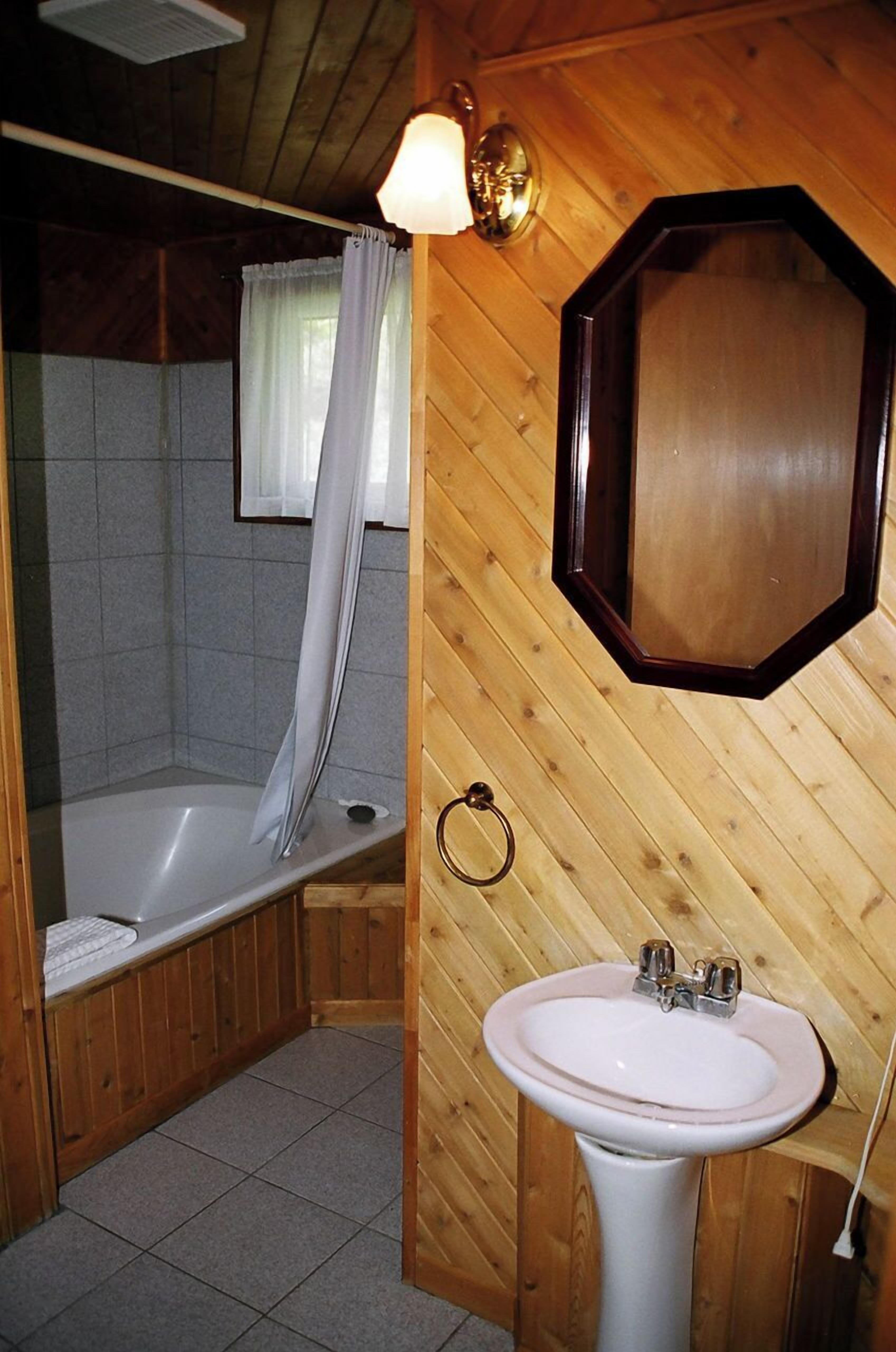 A wooden-paneled bathroom with a bathtub, a sink, and a mirror.
