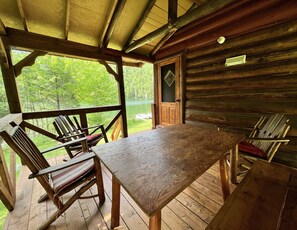 Una baita in legno con un tavolo e sedie sul portico, con vista su un lago.