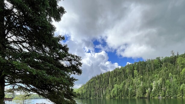 A wooden deck with a view of a lake, surrounded by trees and a cloudy sky. - Kan-à-Mouche Pourvoirie Auberge et Chalets (Saint-Michel-des-Saints)