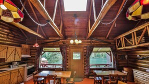 A rustic cabin interior with wooden walls, a dining area with a wooden table and chairs, a kitchen with basic appliances, and a skylight above. - Kan-à-Mouche Pourvoirie Auberge et Chalets (Saint-Michel-des-Saints)
