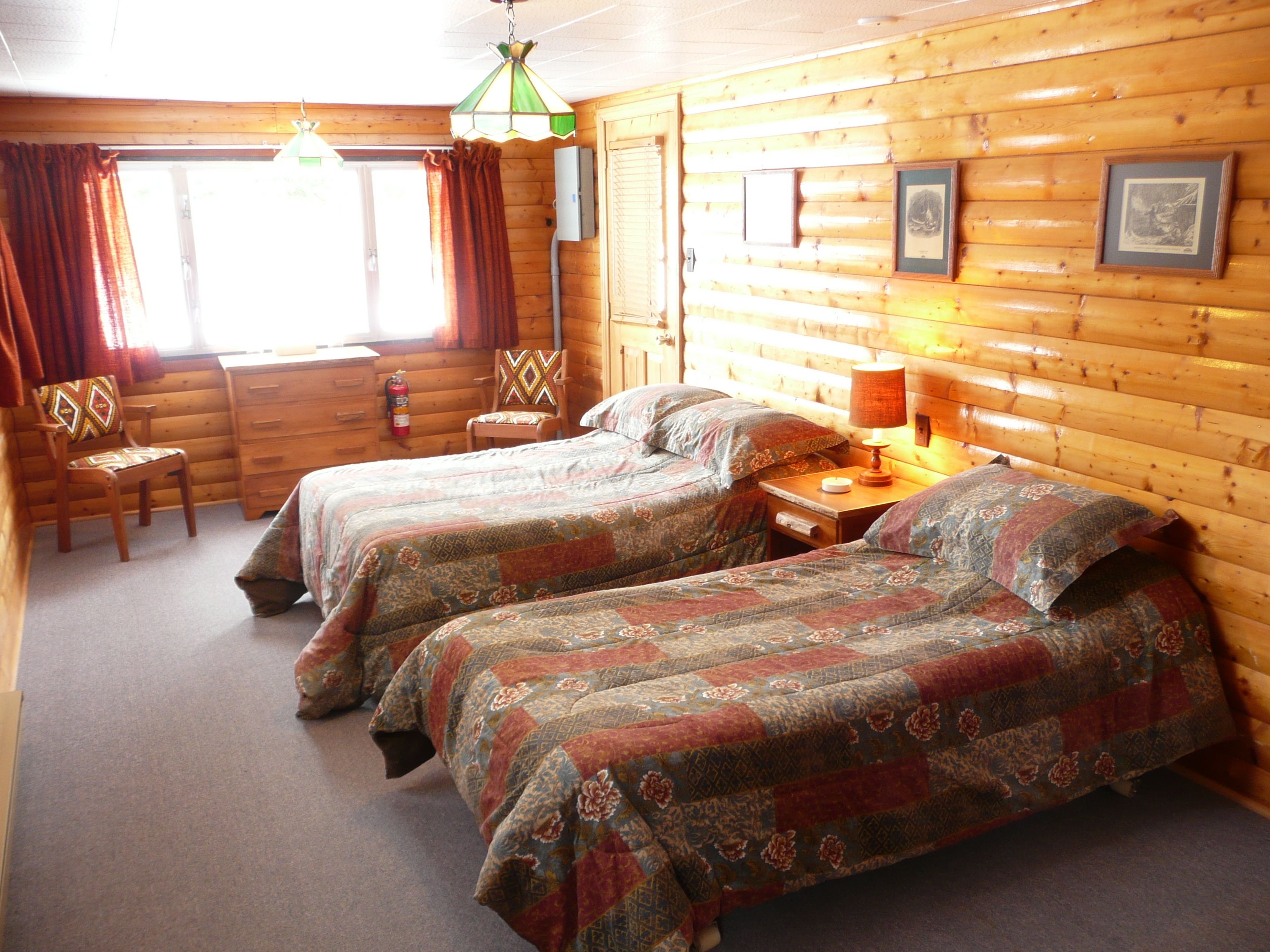 Een kamer in chaletstijl met twee bedden, een stoel, een tafel en een hanglamp.